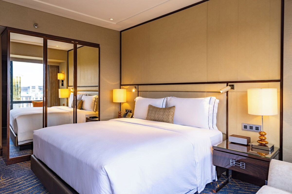 Une chambre d’hôtel avec un grand lit, des tables de chevet, un miroir et une vue sur la ville.