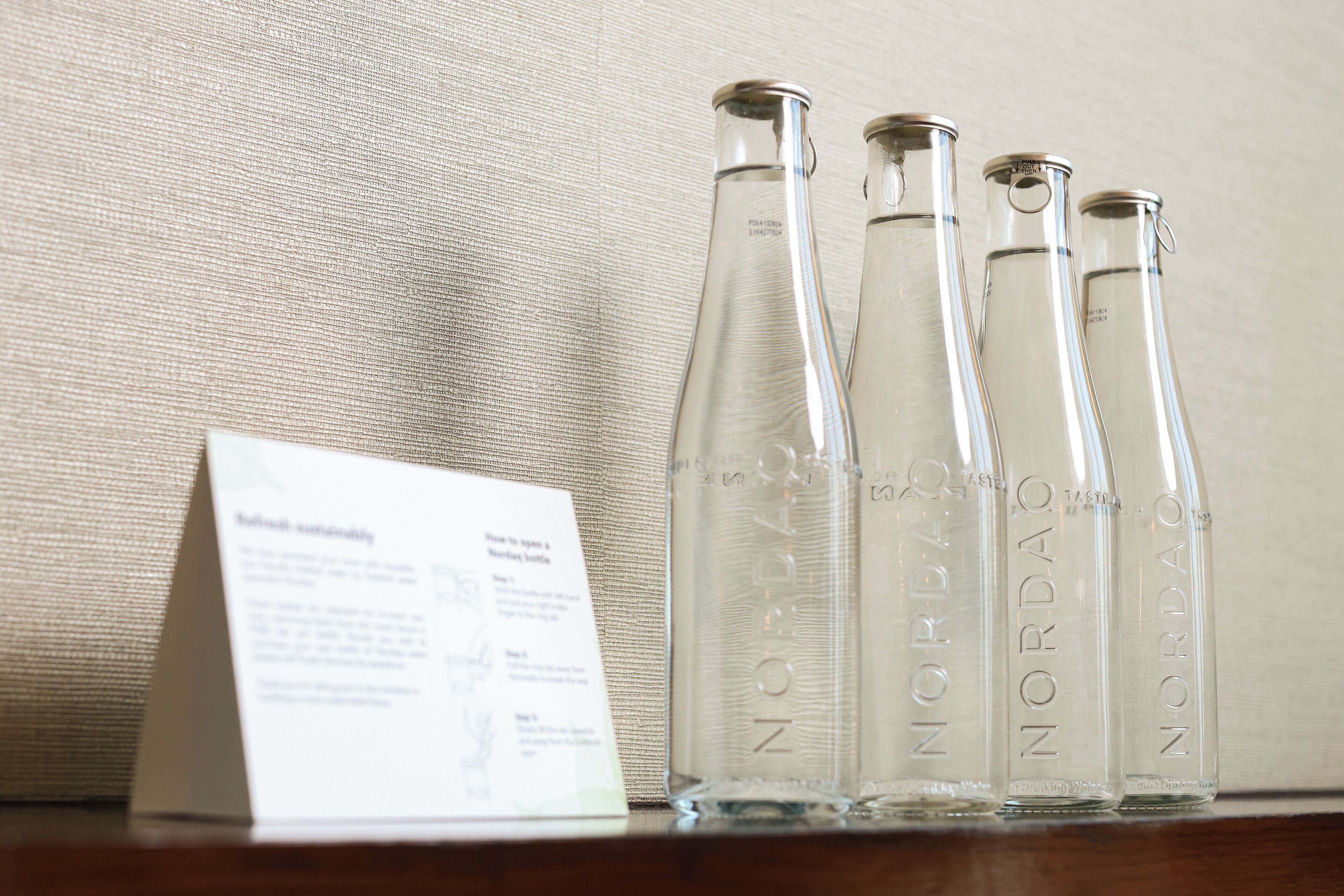 Quatre bouteilles en verre transparent portant l’étiquette « Nordao », posées sur une surface en bois, avec un tissu en arrière-plan.
