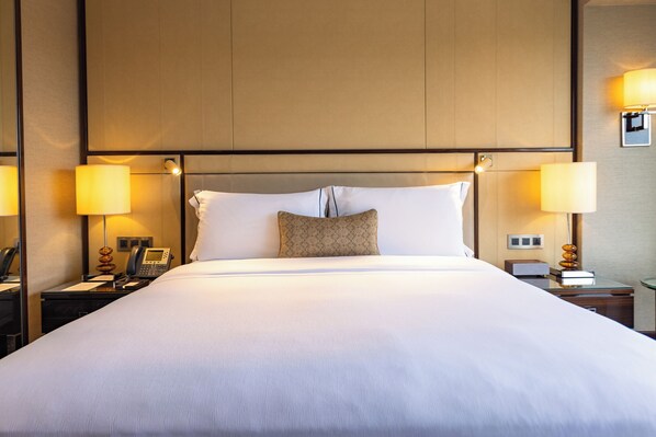 Habitación de hotel con una cama grande, dos lámparas de noche, un teléfono y una mesita con lámpara.