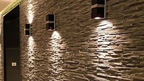 A hallway with a textured stone wall, recessed lighting, and a plant.