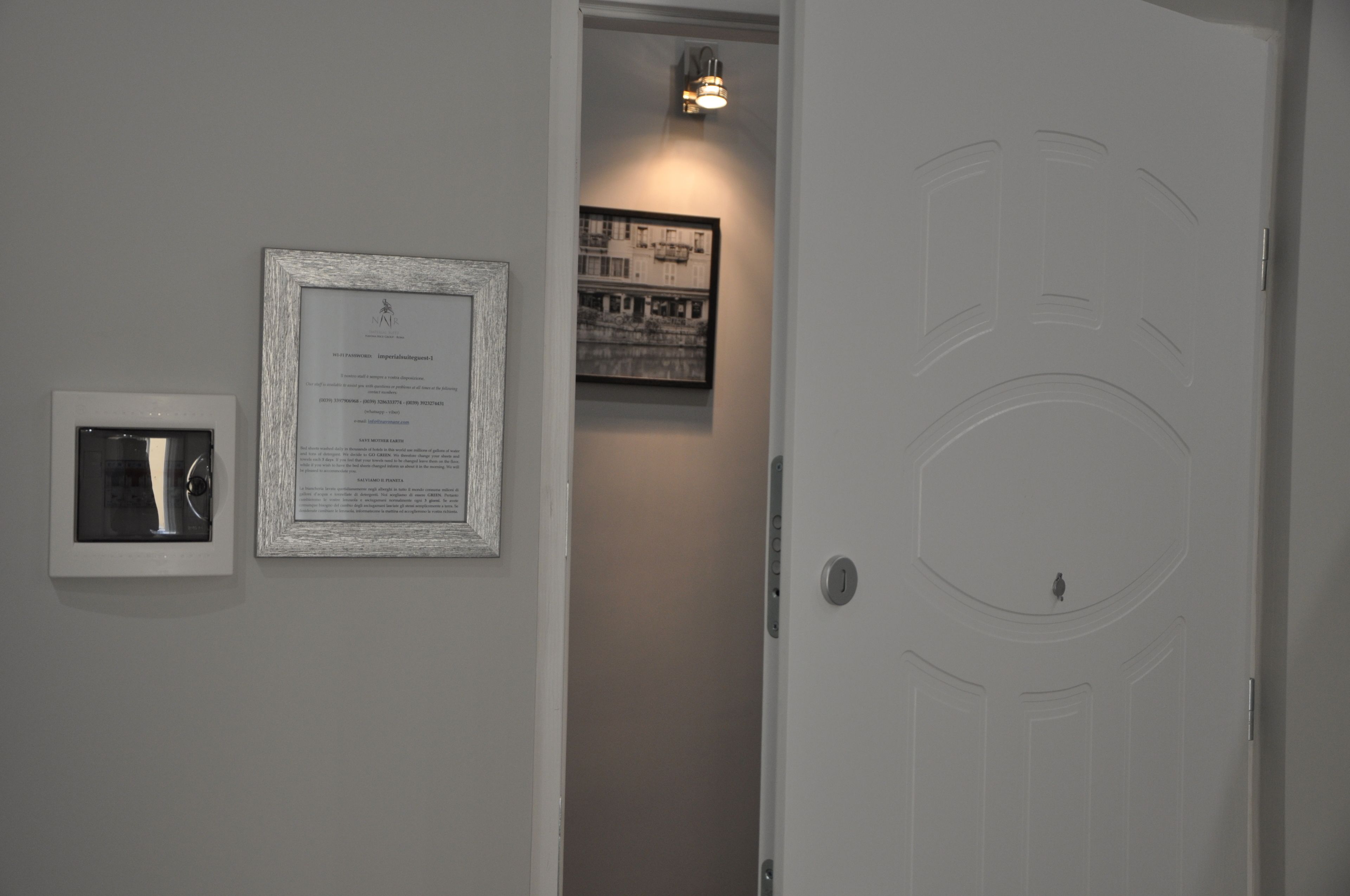 Un couloir avec un certificat encadré accroché au mur, une photographie encadrée et une porte dotée d’un trou de serrure.