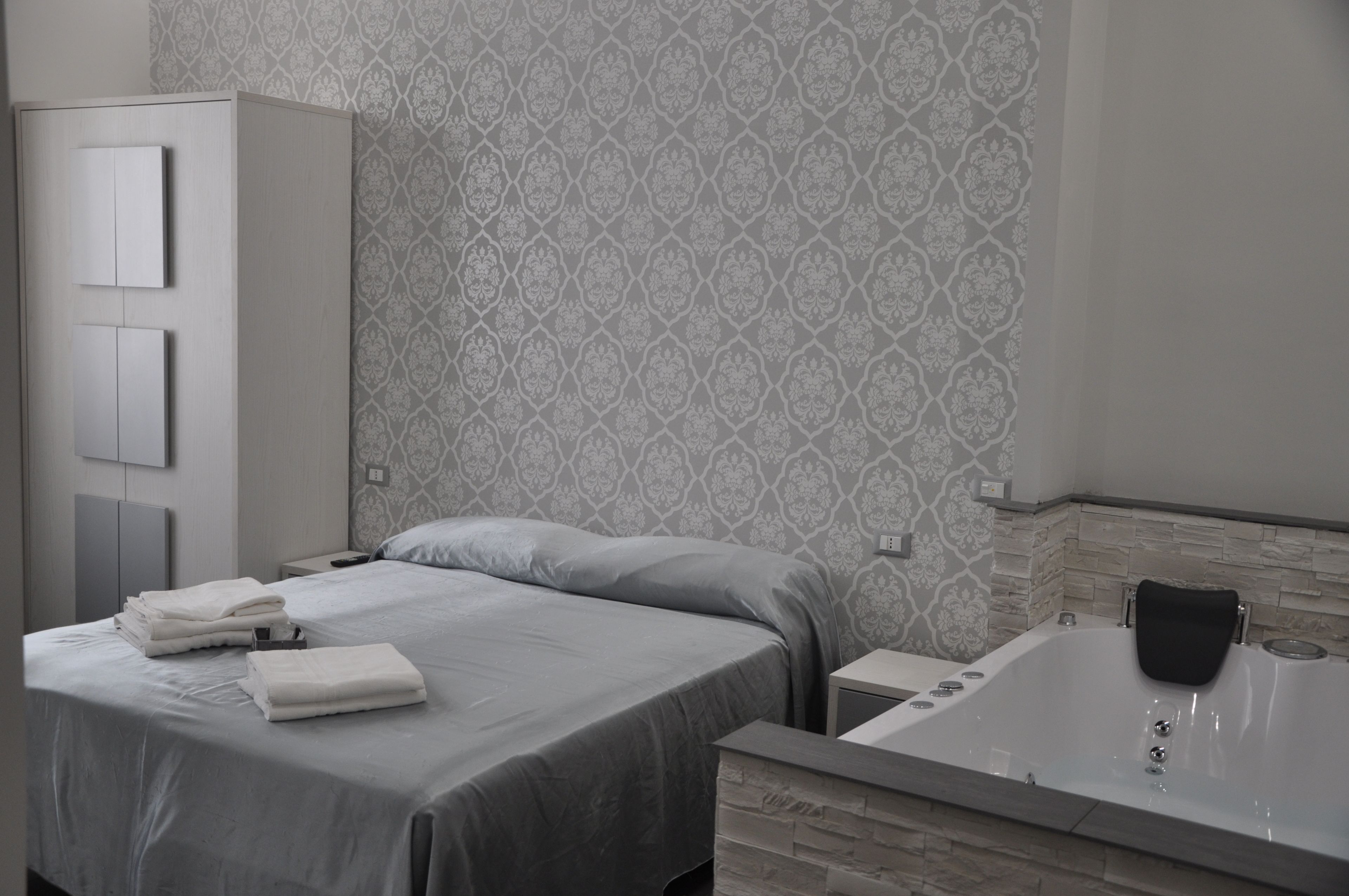 A modern hotel room with a neatly made bed, a large bathtub, and a wardrobe.