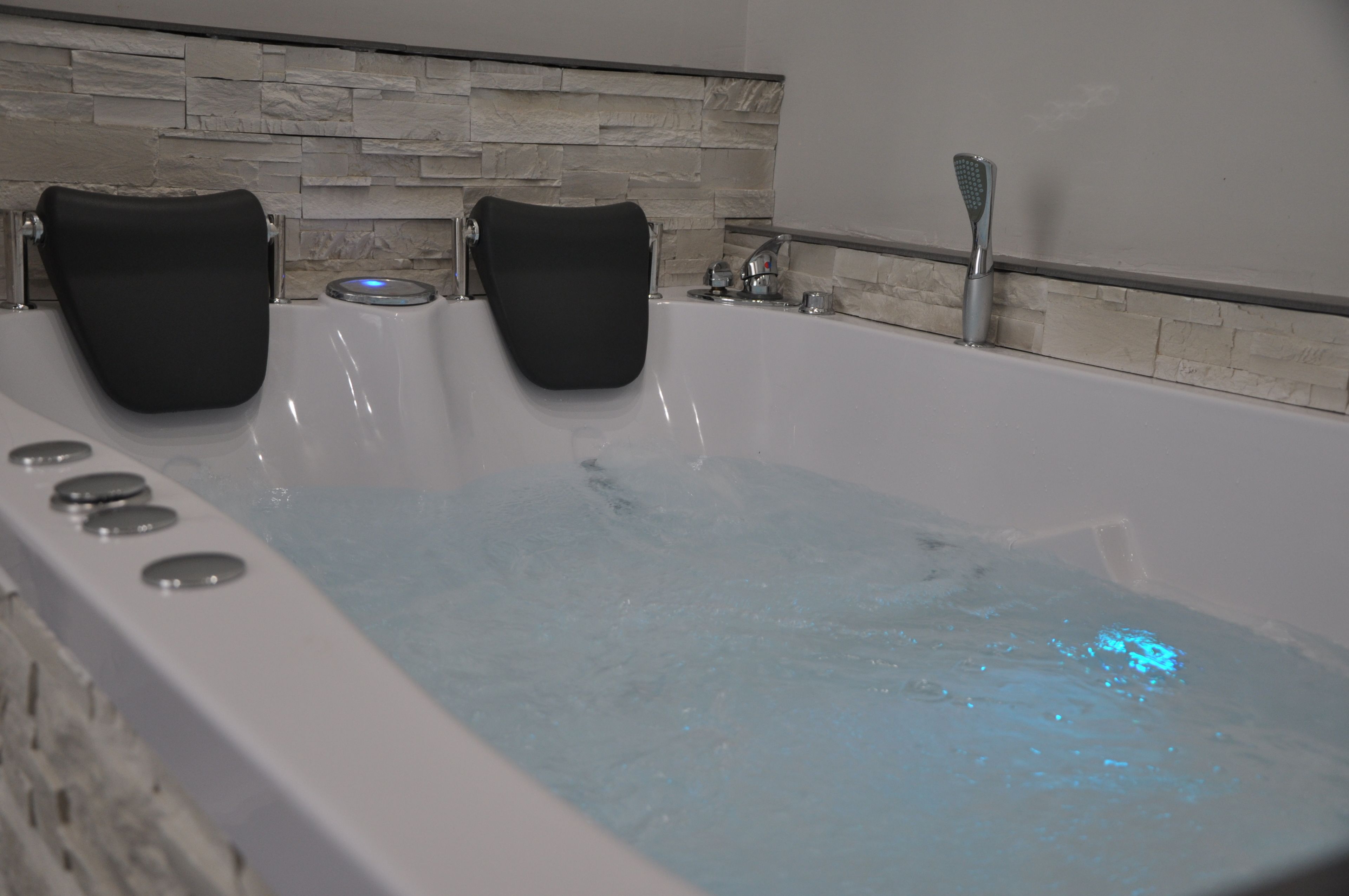 Un baño moderno con una bañera grande, dos toallas negras y una pared de piedra.