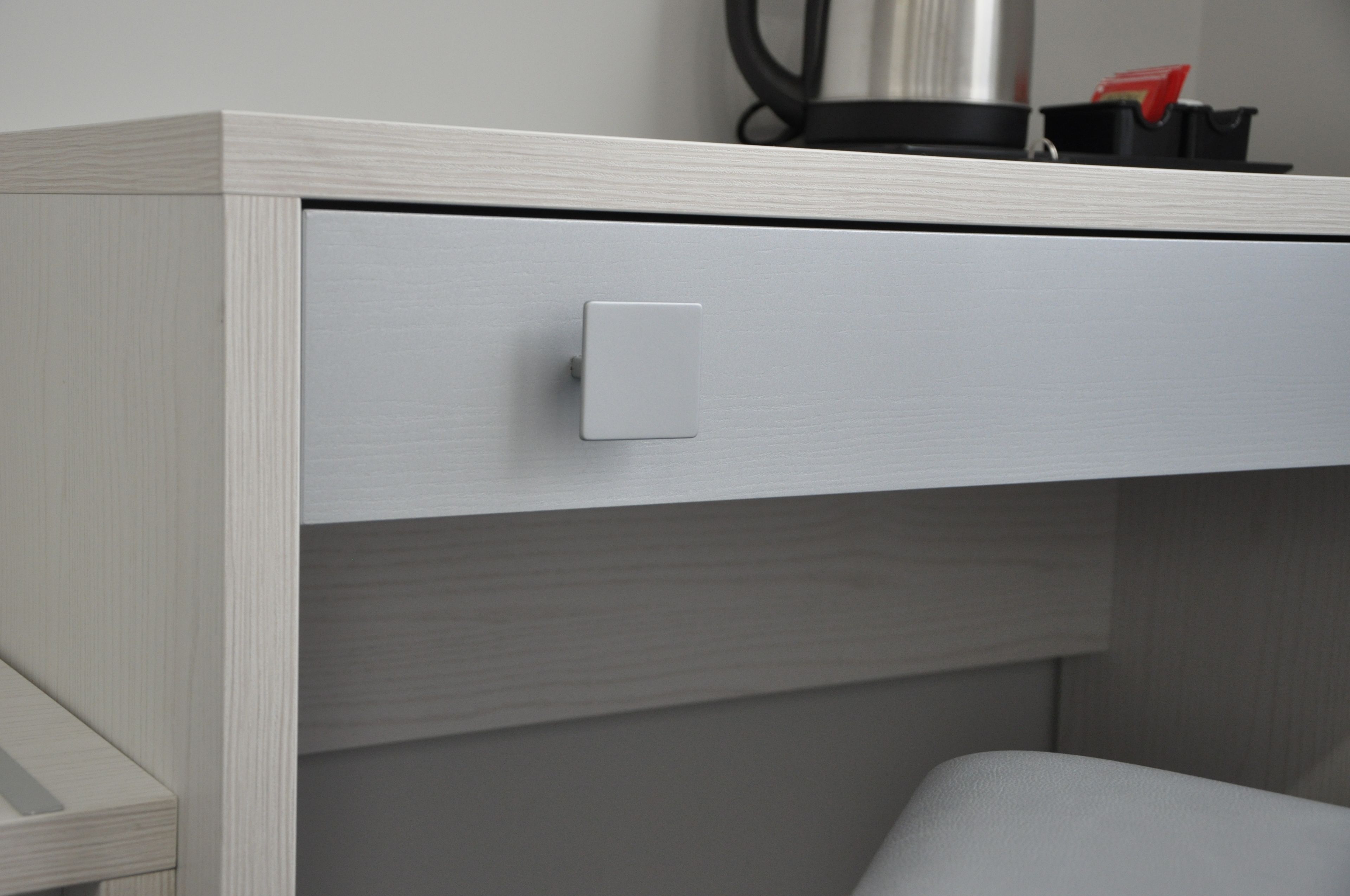Een witte kast met een lade, een lichtschakelaar en een zwart voorwerp erboven.