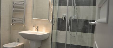 A modern bathroom with a glass-enclosed shower, a pedestal sink, a bidet, and a towel rack.