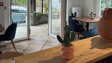 Een hotelkamer met een houten bureau, een cactusplant, een koffiezetapparaat en uitzicht op het buitenterras.