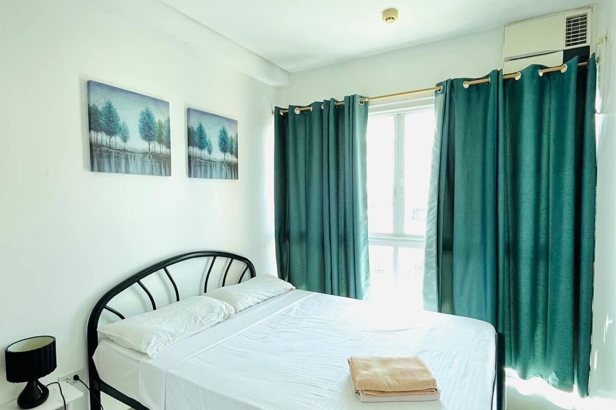 A bedroom with a bed, a nightstand, two wall art pieces, and a window with curtains.