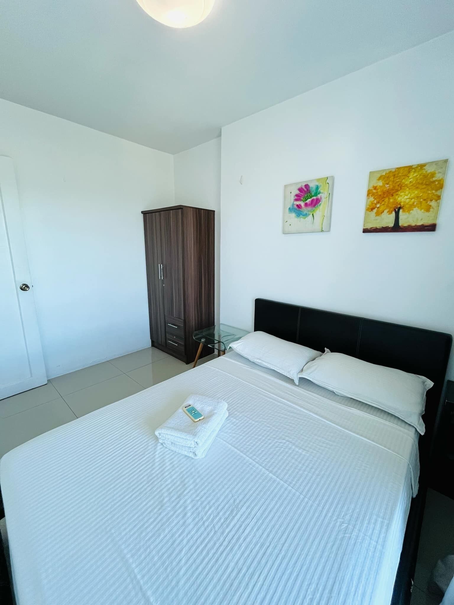A hotel room with a bed, a wardrobe, and two paintings on the wall.