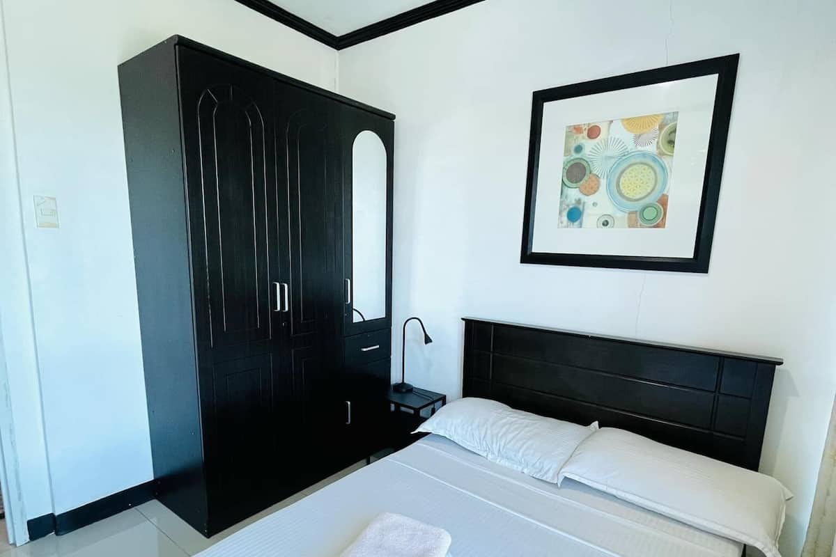 A modern bedroom with a large bed, a dark wardrobe, and a framed picture on the wall.