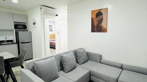 A modern living room with a grey sectional sofa, a dining area with a table and chairs, and a kitchen area with appliances. - Primavera Residences (Cagayan de Oro)