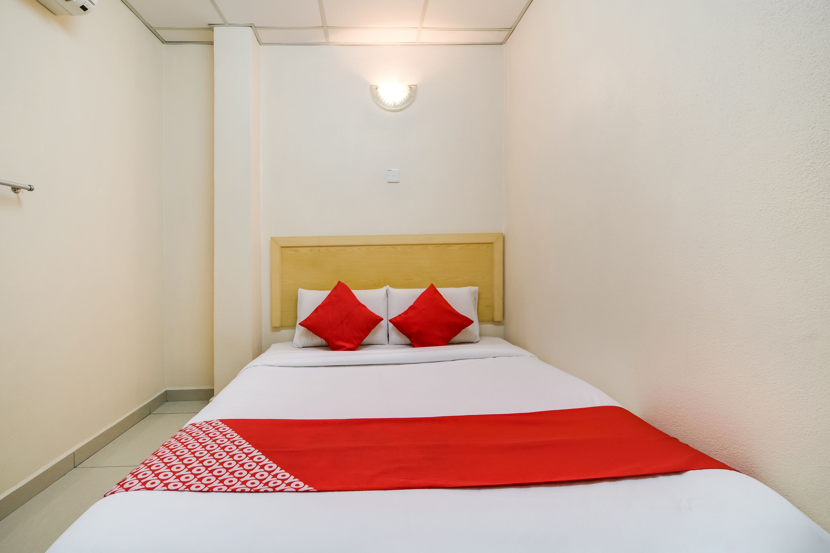 A hotel room with a bed, a headboard, and a red and white bedspread.