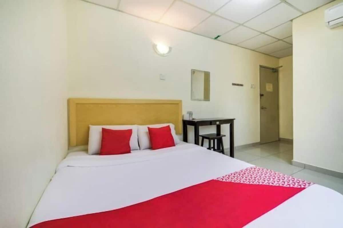 Hotellihuone, jossa on sänky, puinen pääty, pieni pöytä ja peili seinällä.
