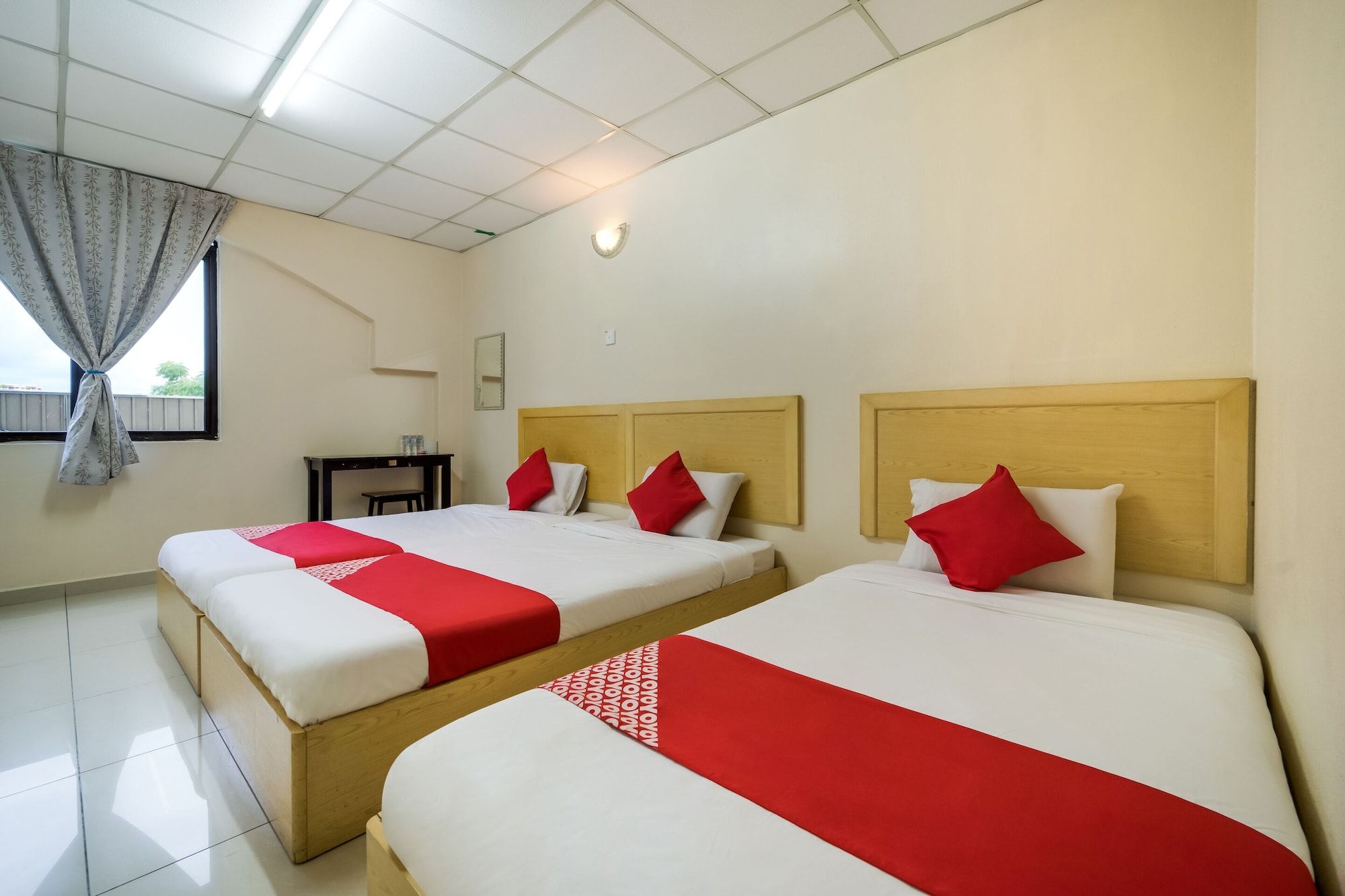 A hotel room with two beds, each with a wooden headboard, white bedding, and red accents.