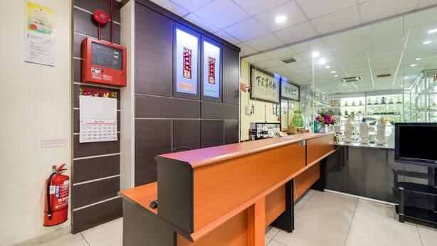 A reception area with a wooden bench, a fire extinguisher, a digital display, and a calendar on the wall. - River Inn Hotel (Butterworth)