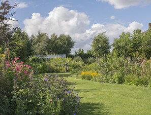 A lush garden with a variety of flowers and a greenhouse in the background. - De Sfeerstal (Nieuwveen)