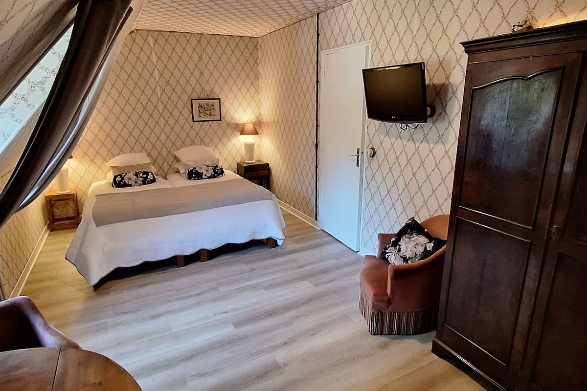 Un dormitorio con cama, televisión montada en la pared, armario de madera y una silla.