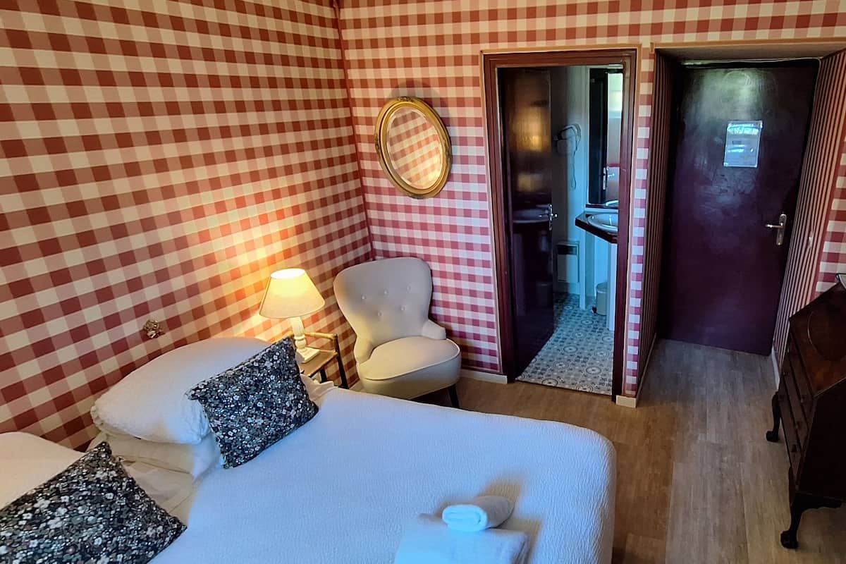 Una habitación de hotel con un estampado de cuadros en la pared, una cama con almohadas, una silla, un aparador, un espejo y un televisor en la pared.