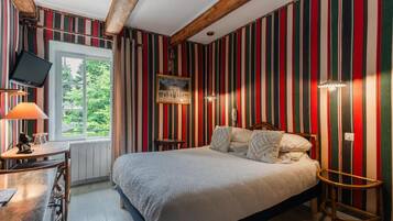 Een kamer met een bed, een bureau, een stoel, een televisie en een raam met uitzicht op groen.