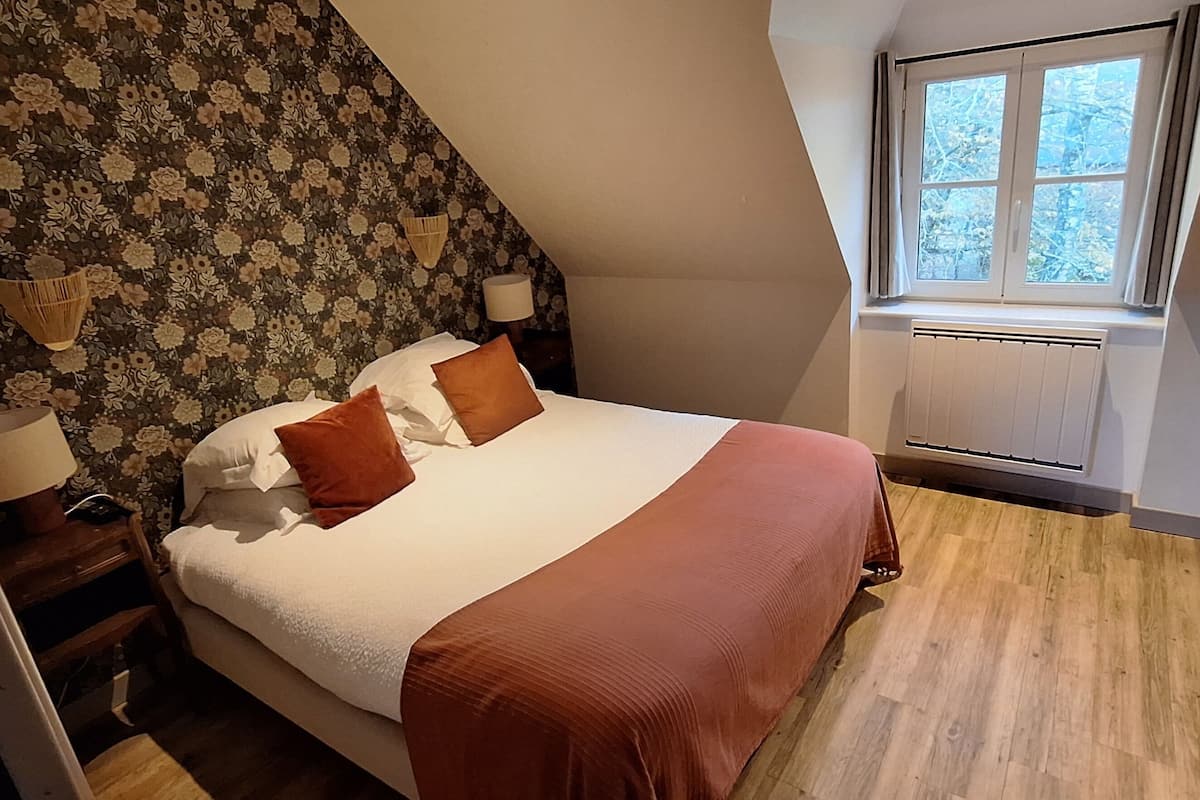 Un dormitorio con cama, mesita de noche, ventana y radiador.