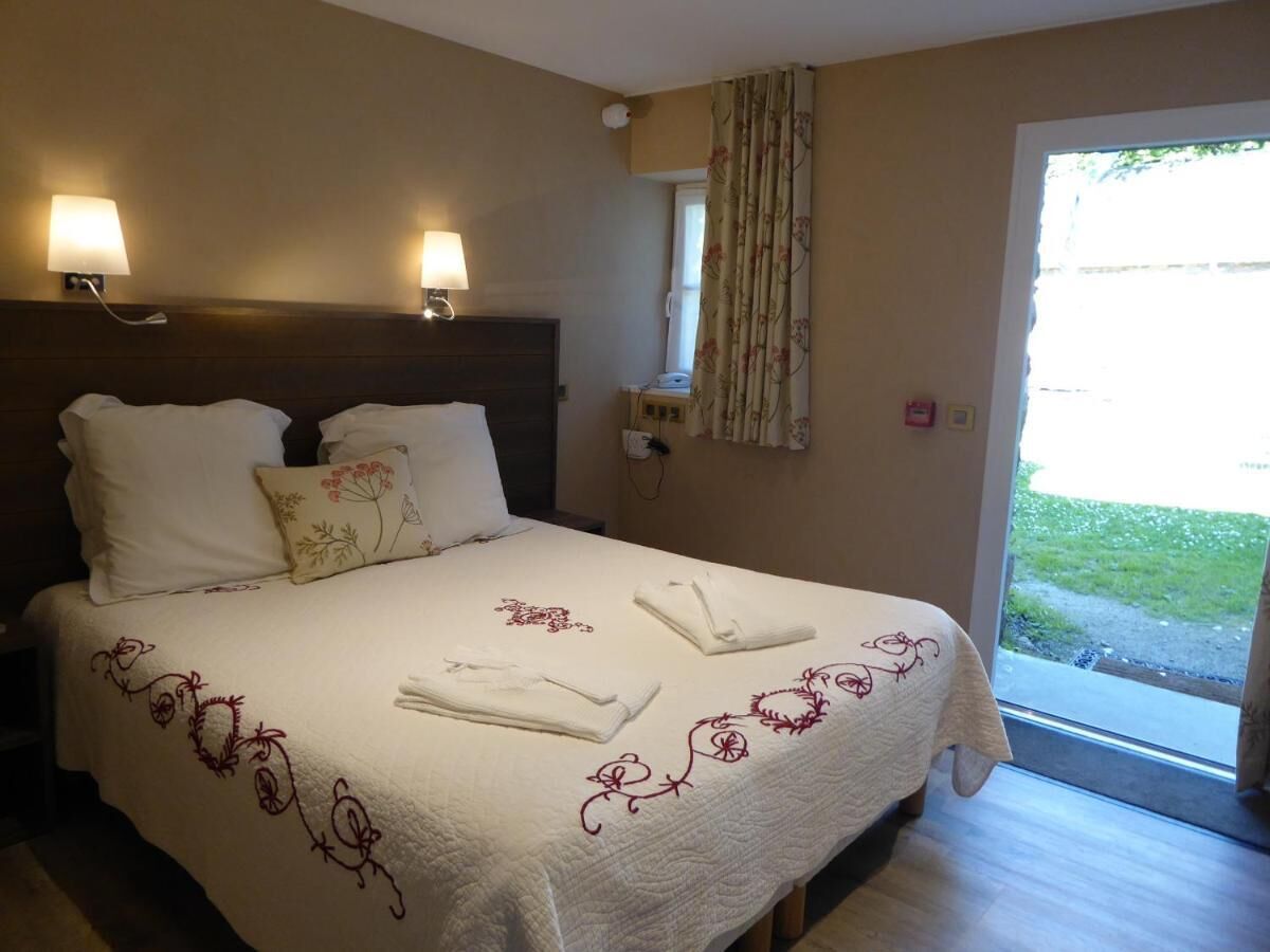 Een hotelkamer met een bed, twee wandlampen, een raam met gordijnen en uitzicht op de omgeving.