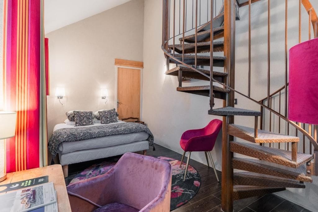 Un dormitorio con cama, una silla, una escalera de madera y una puerta.