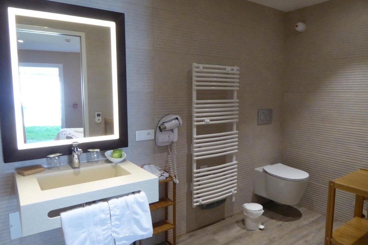 A modern bathroom with a large mirror, a sink, a toilet, and a towel rack.