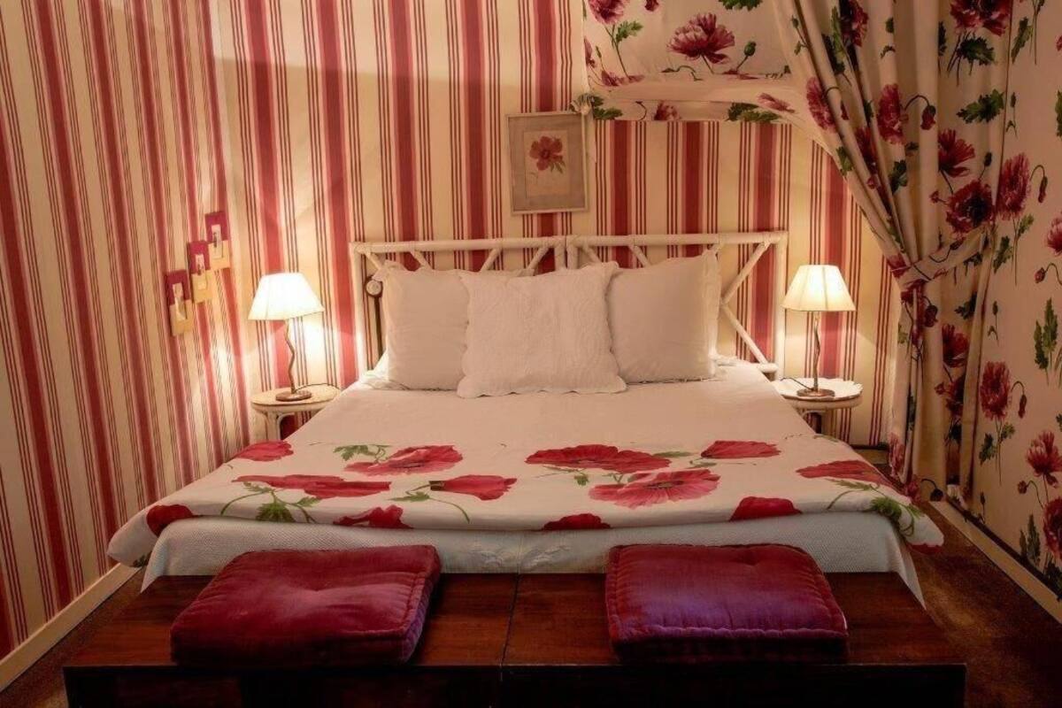 Una cama con una colcha estampada, papel tapiz a rayas y dos lámparas de noche.