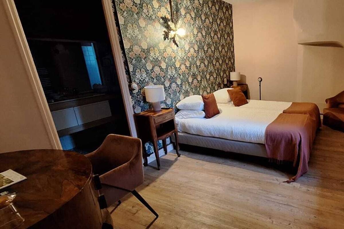 Habitación de hotel con cama, escritorio, silla, radiador y pared con estampado floral.