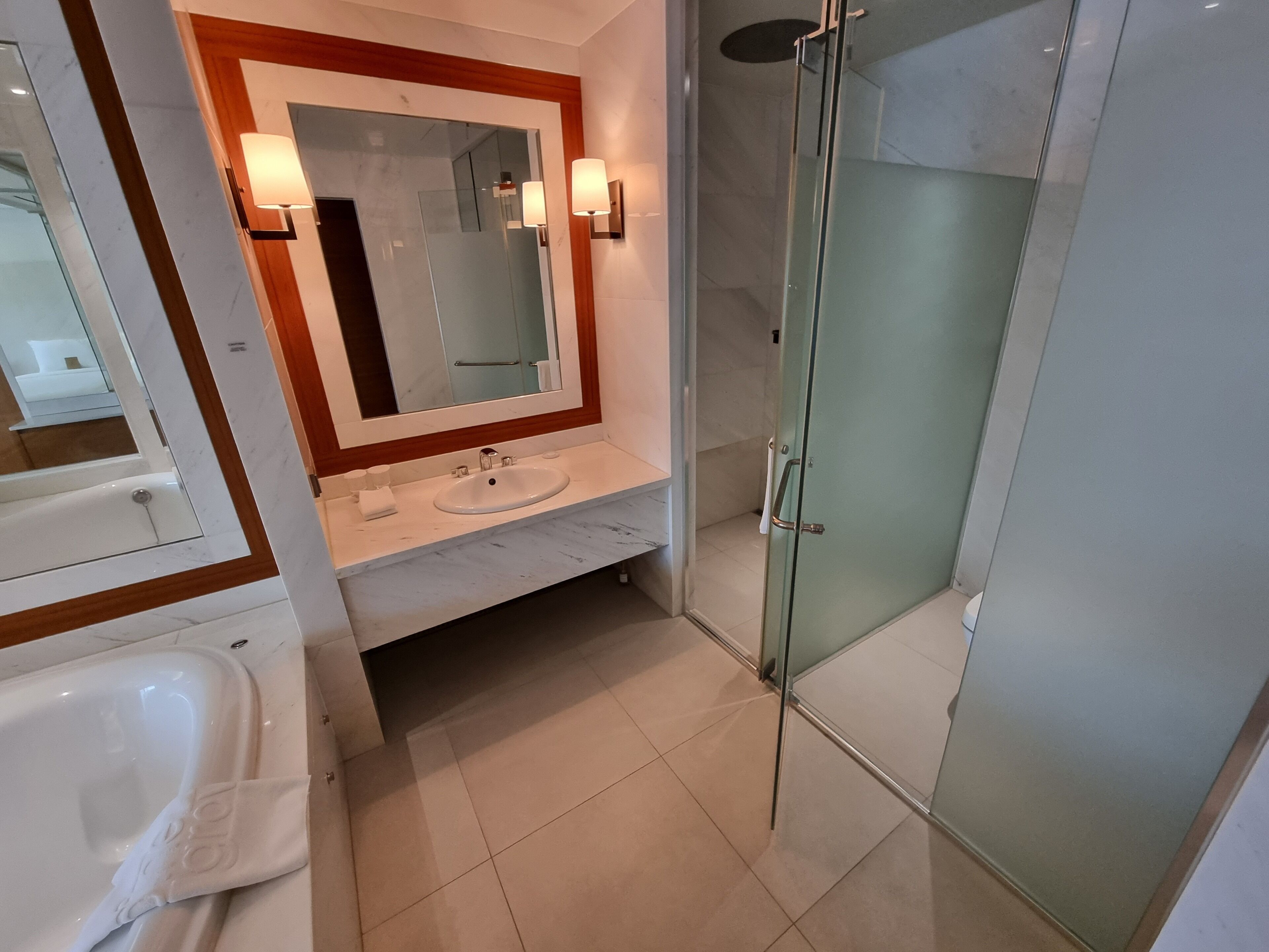 Une salle de bain moderne avec une douche à parois de verre, un lavabo blanc et un grand miroir agrémenté d’appliques murales.
