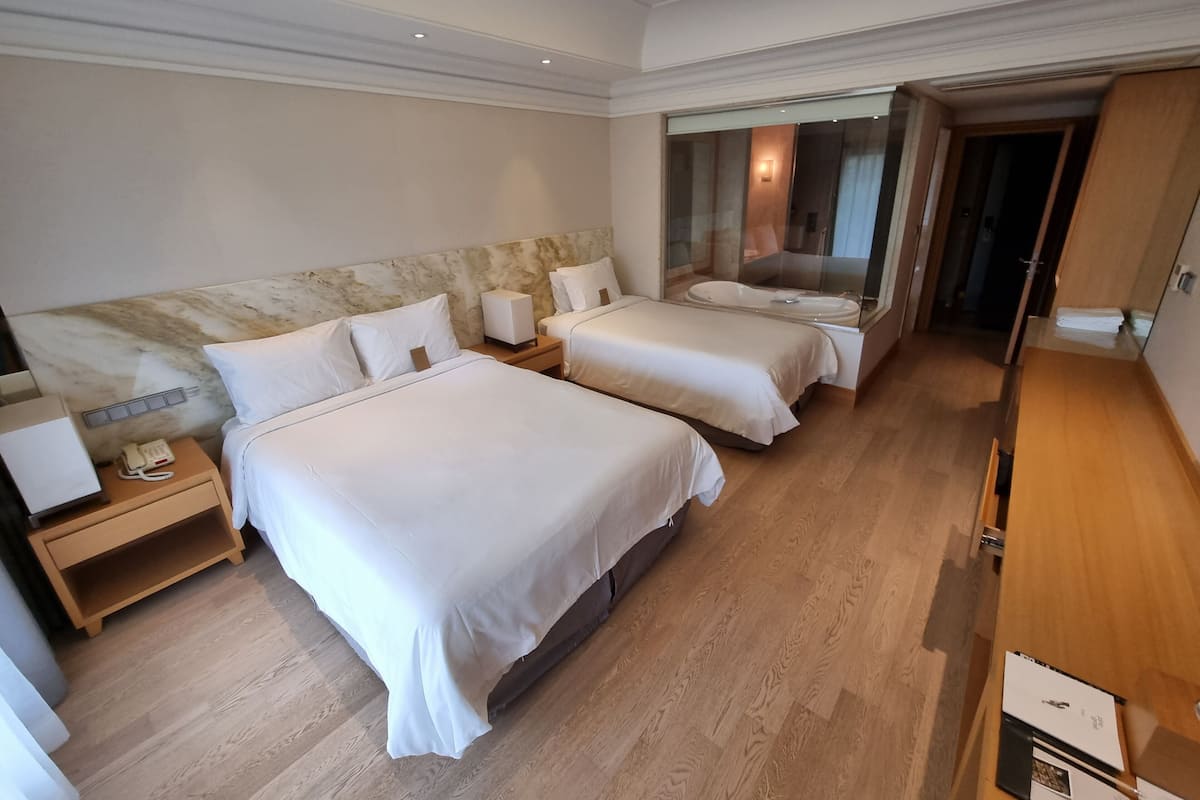 Habitación de hotel con dos camas, cabecera de mármol, mesita de noche con lámpara, teléfono y suelo de madera.