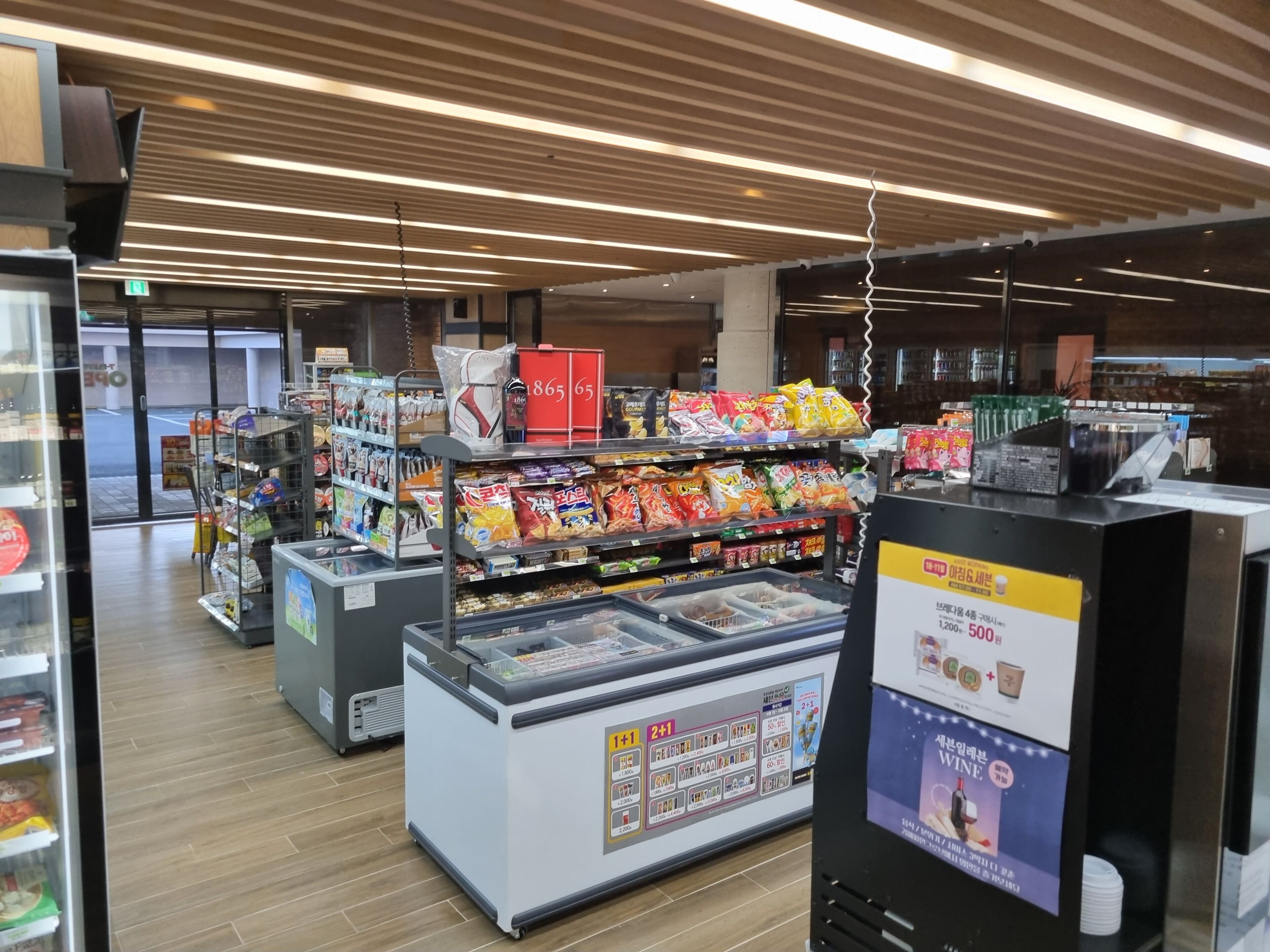 A grocery store interior with refrigerated sections, shelves stocked with snacks, and a checkout area.