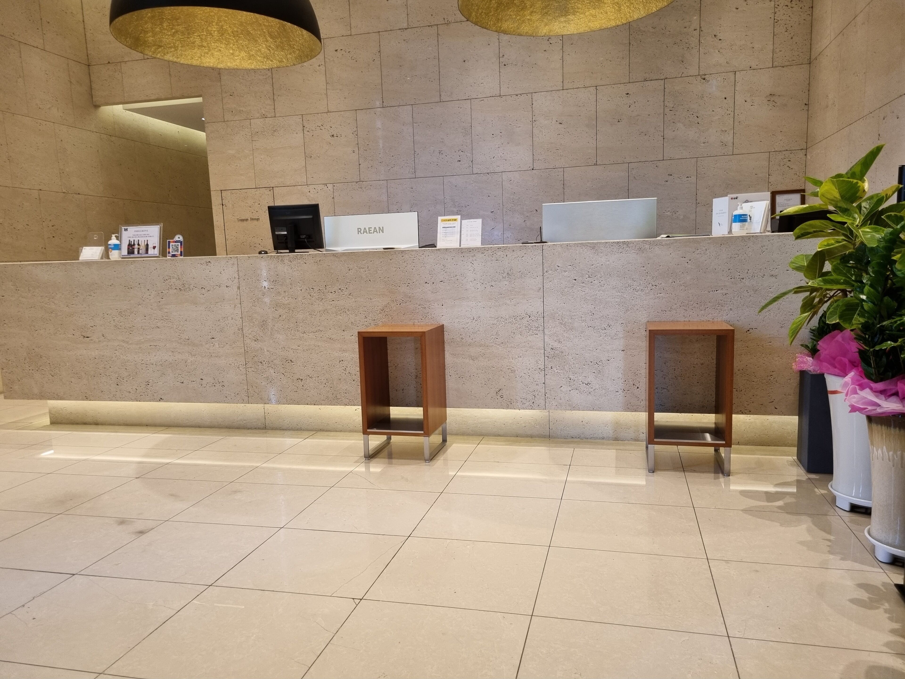 A reception area with a marble wall, two wooden stools, a reception desk, and a potted plant.