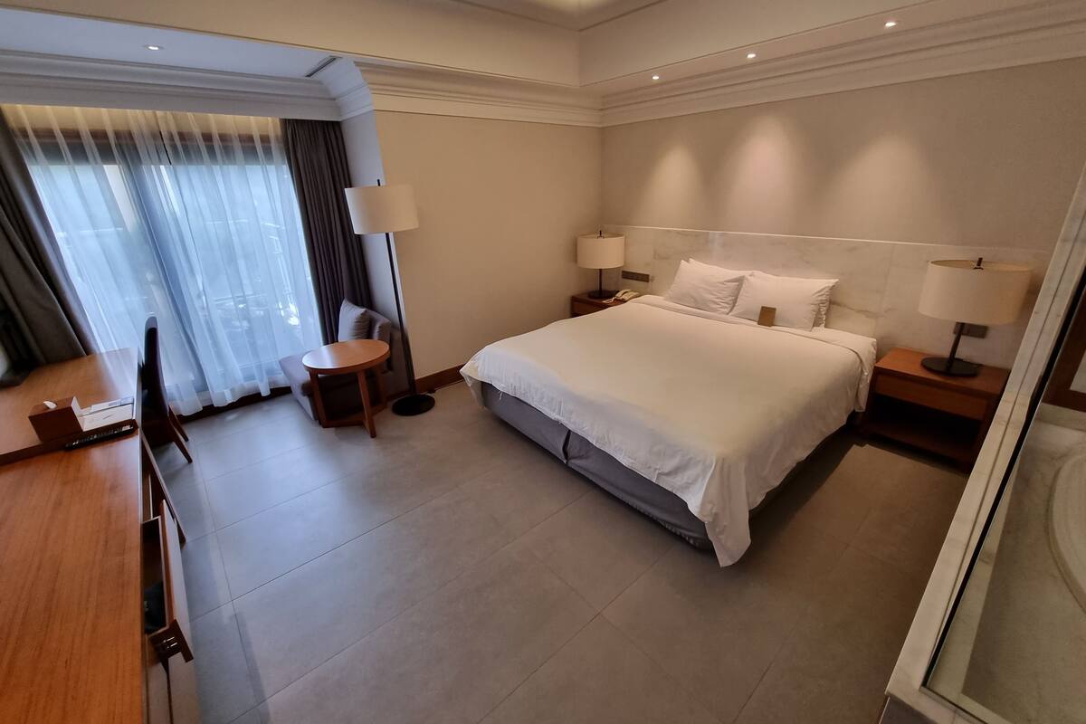 Una habitación de hotel con una cama grande, mesitas de noche con lámparas, una pequeña mesa redonda y una silla.