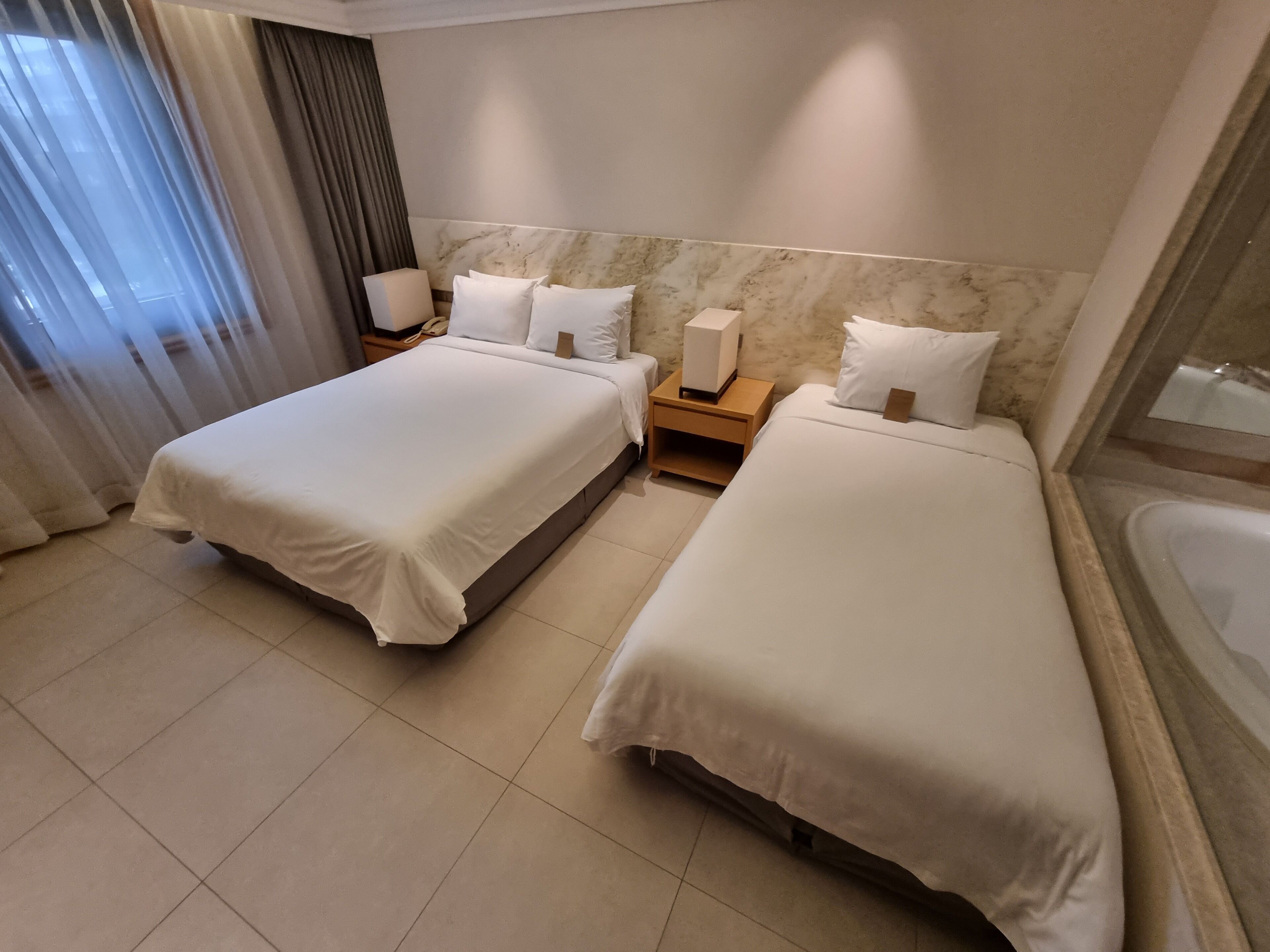 A hotel room with two beds, a bathroom, and a large window with curtains.