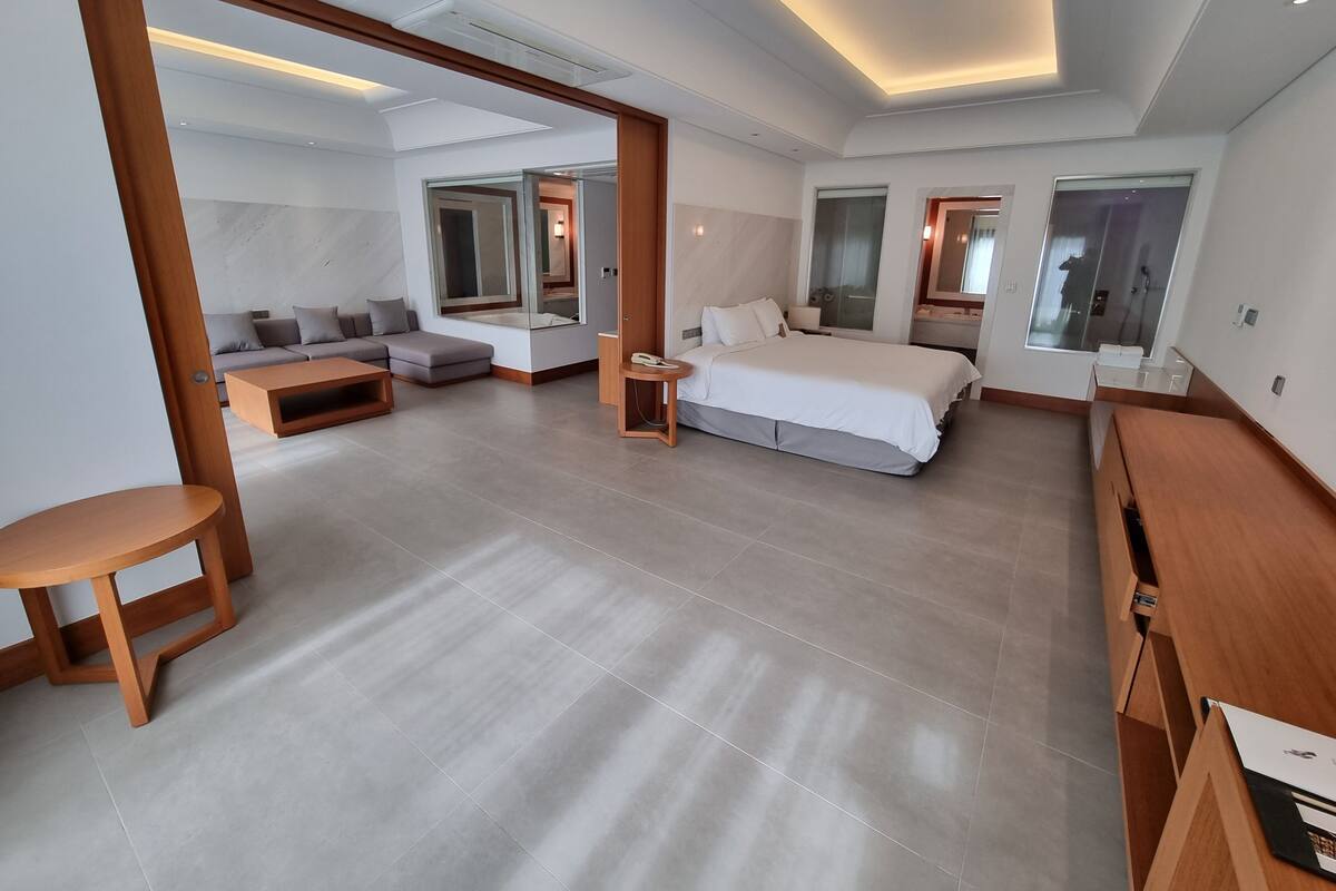 Una habitación de hotel moderna con una cama grande, un sofá, una mesita y un espejo.