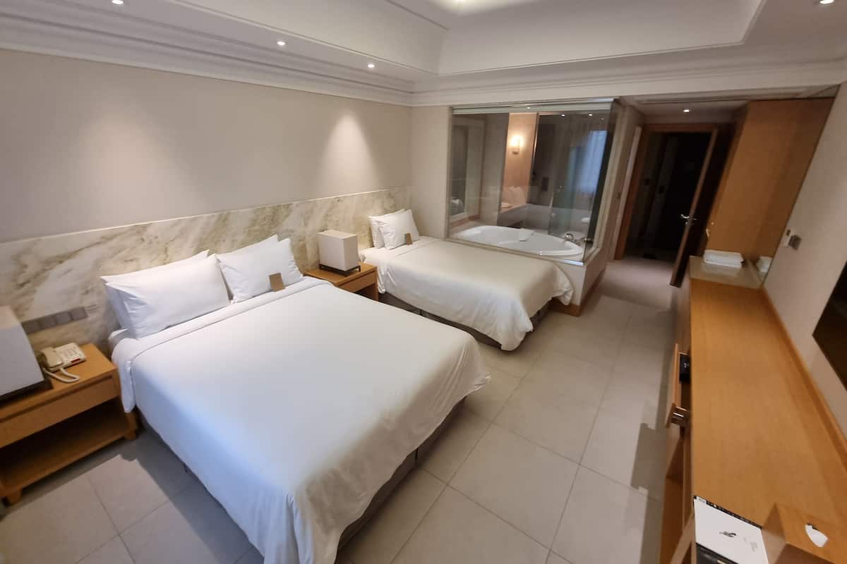 Habitación de hotel con dos camas, baño con cabina de ducha de vidrio y cómoda de madera.