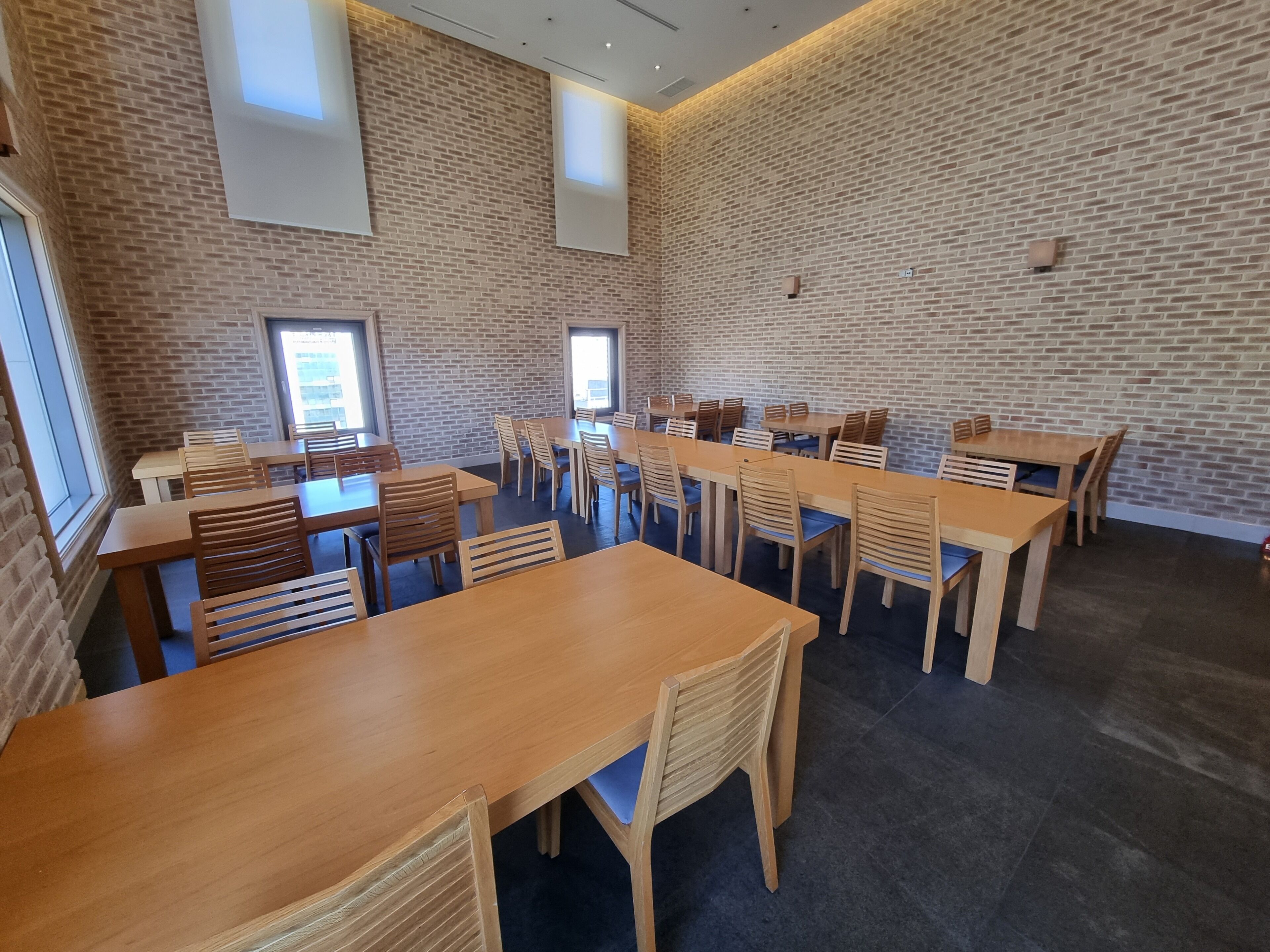 Un salón de conferencias con paredes de ladrillo, varias mesas y sillas dispuestas para reuniones.