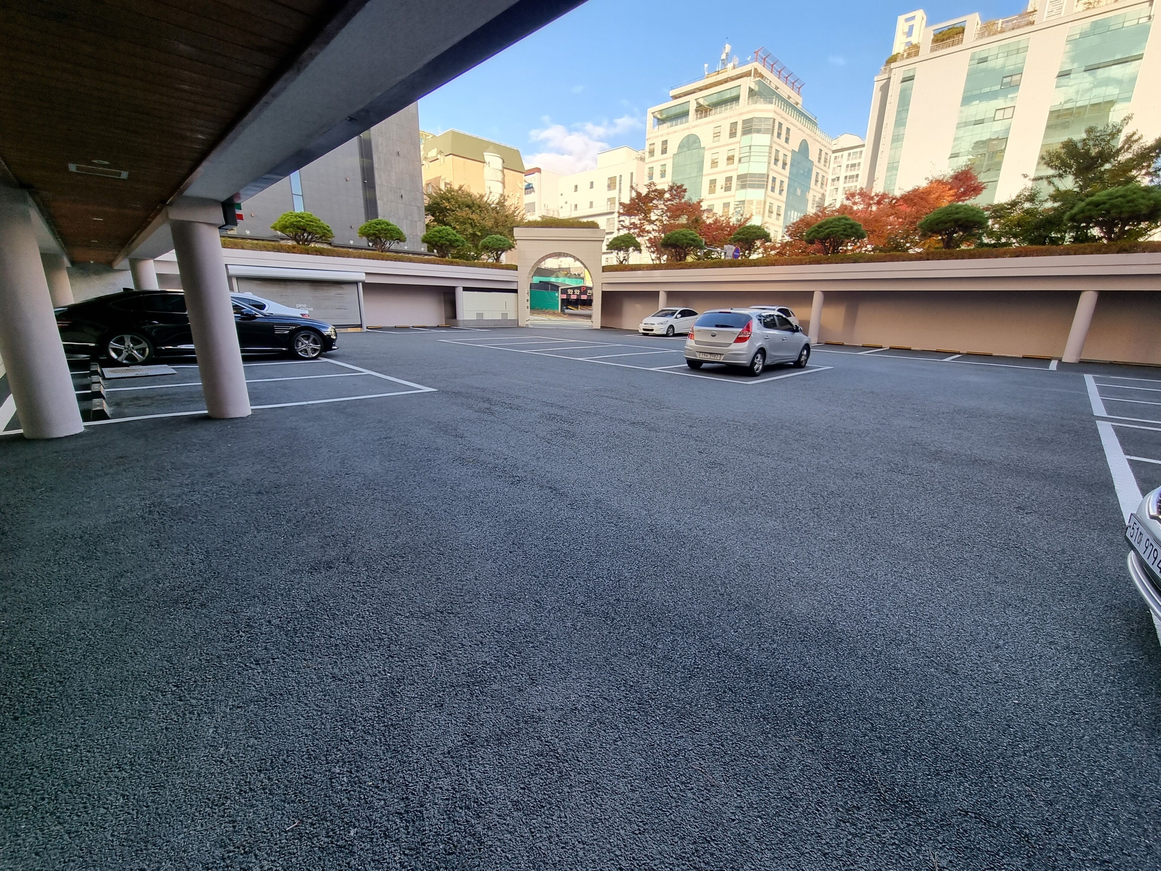 A parking area with cars, a covered walkway, and buildings in the background.