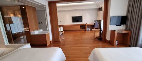 Habitación de hotel con dos camas, un escritorio, una silla, un televisor y un espejo grande.