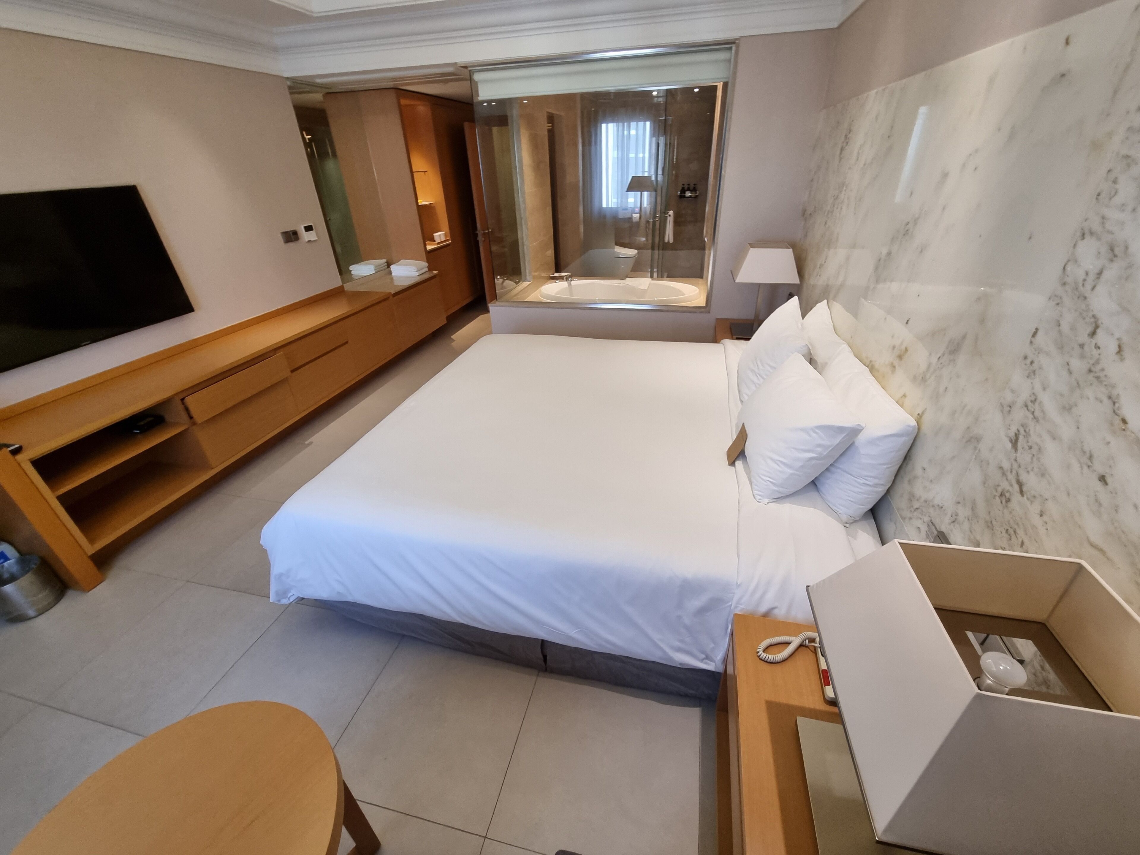 Een hotelkamer met een groot bed, een televisie, een houten bureau en een badkamer zichtbaar door een glazen deur.