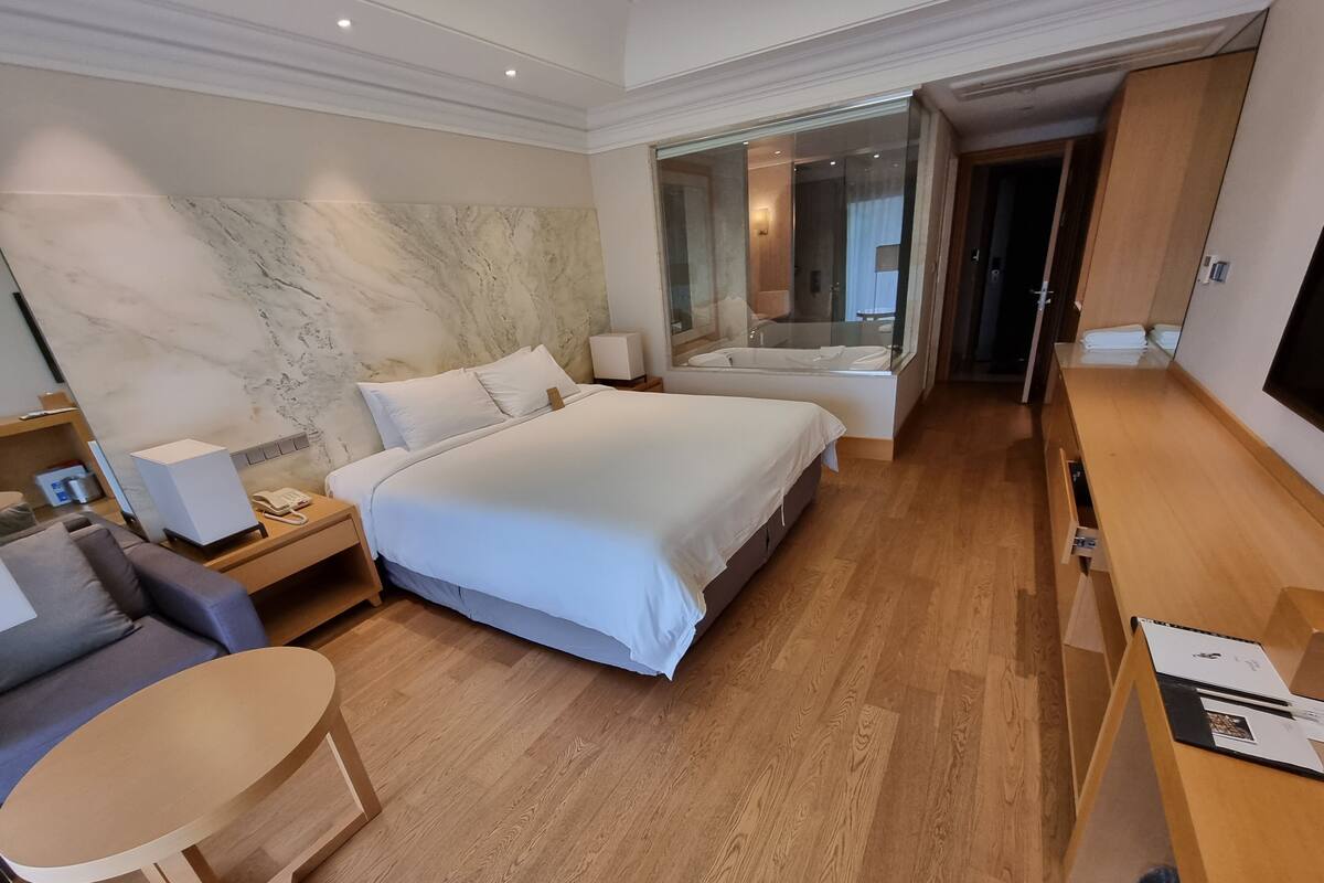 Habitación de hotel con una cama grande, un escritorio, una silla, un sofá, un televisor y un baño con bañera y ducha.