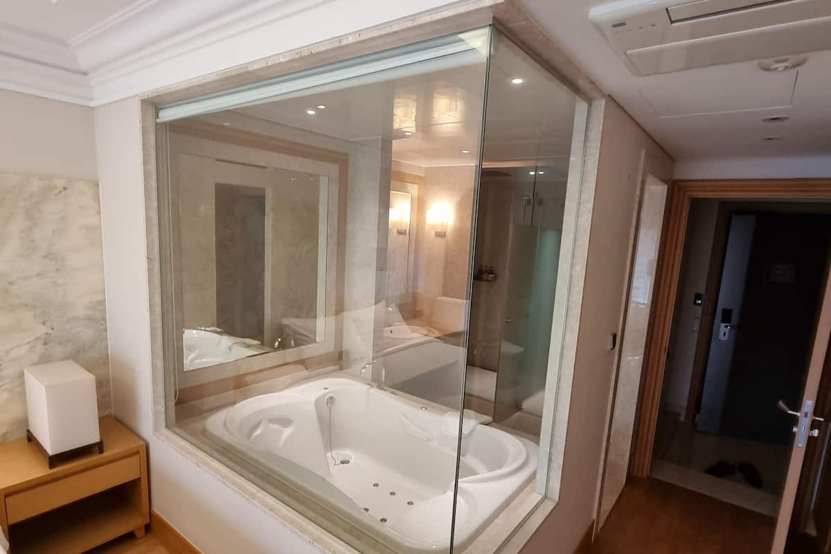 Un baño moderno con un jacuzzi de vidrio, tocador de madera y pared de mármol.