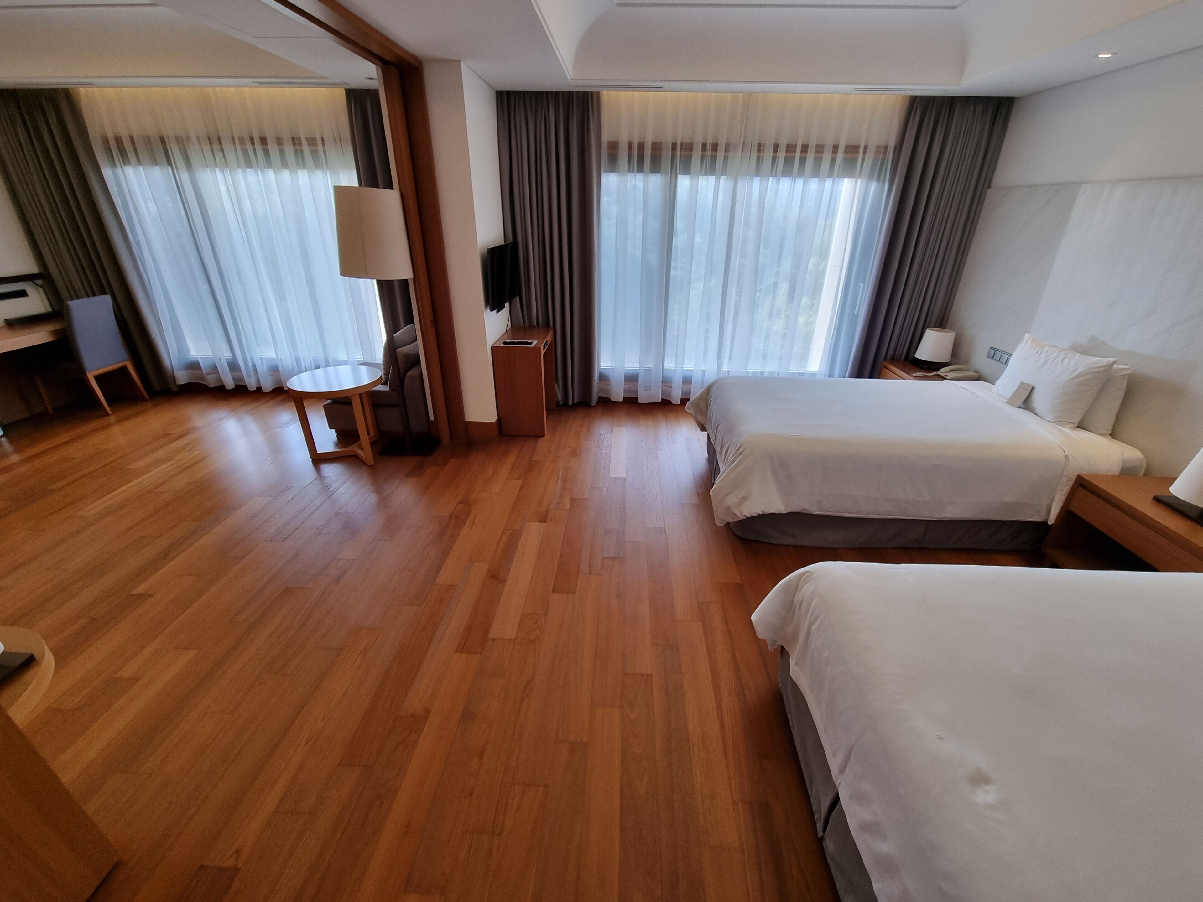 Una camera d'albergo con due letti, una scrivania, una sedia, una TV e ampie finestre con tende.