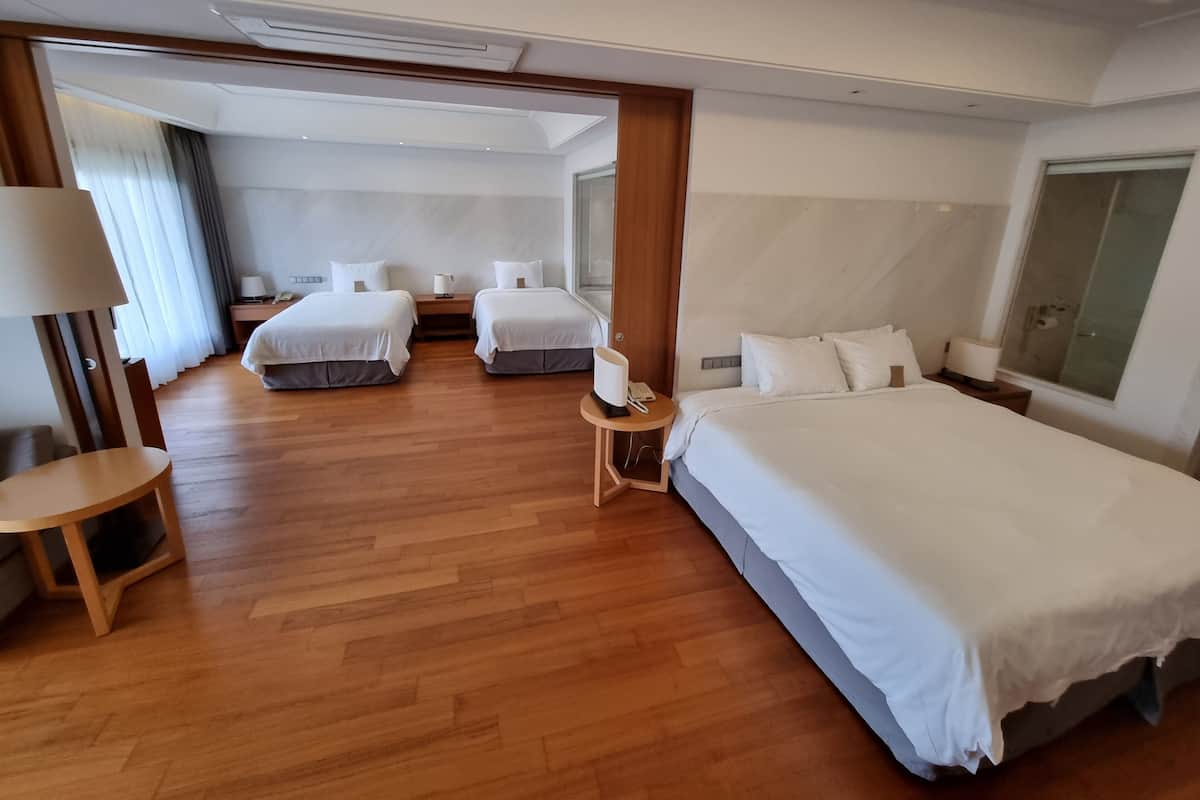 Habitación de hotel con una cama grande, dos camas más pequeñas, suelo de madera, un escritorio y una lámpara.