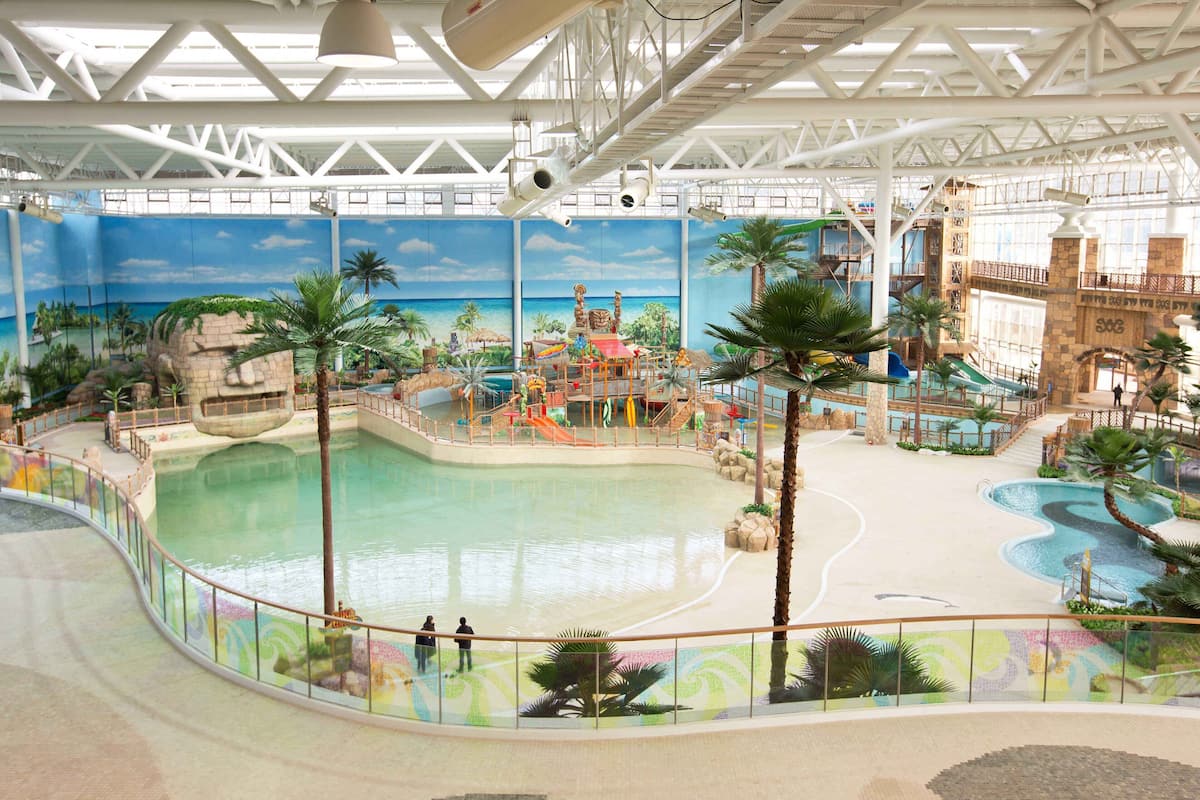 Parque aquático interno com uma piscina grande, toboáguas e tema tropical.