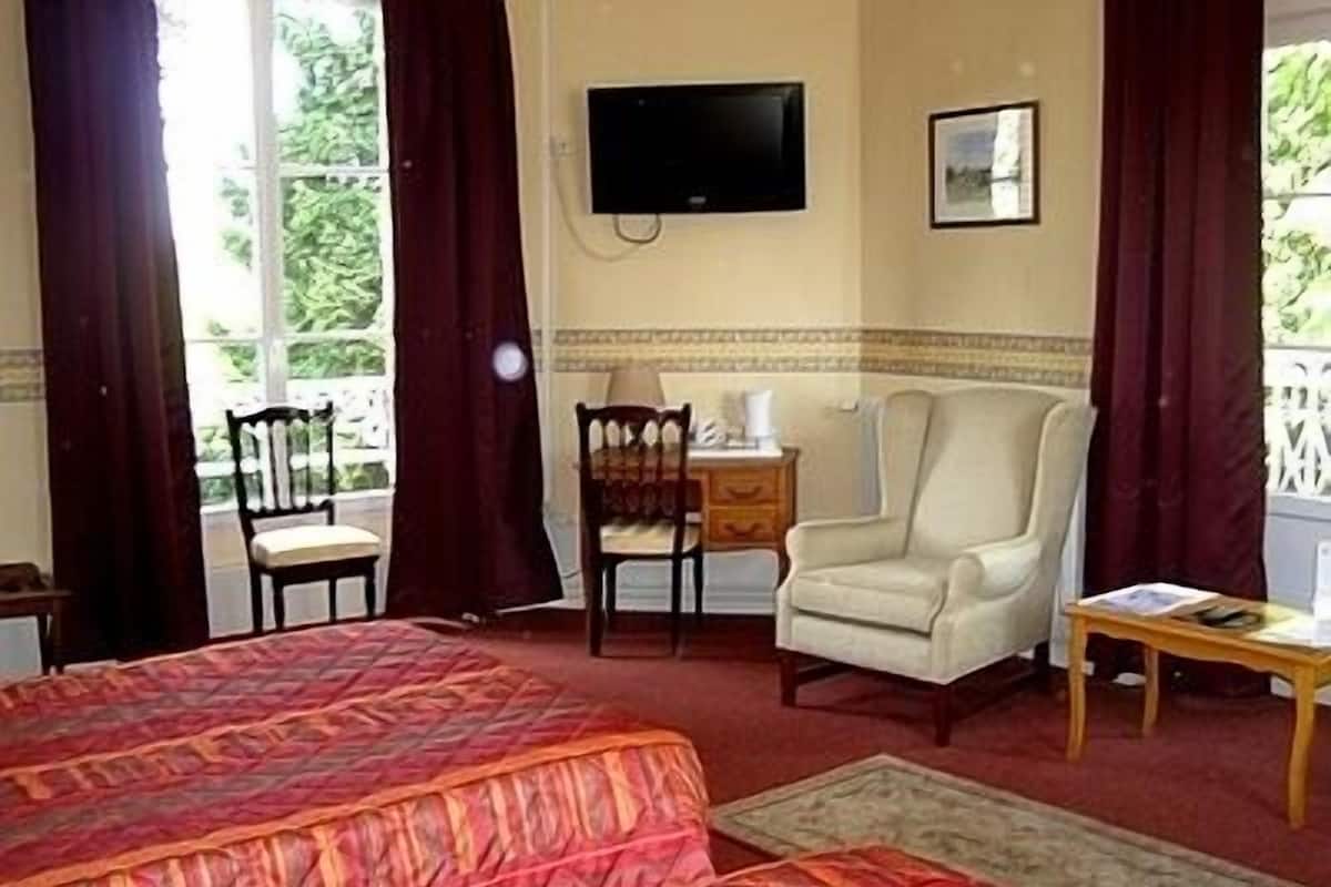 A hotel room with a large bed, a desk, a chair, a television, and a window with curtains.