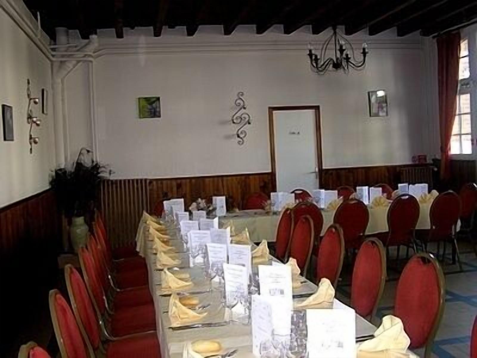 Une salle de conférence avec une longue table préparée pour une réunion, des chaises rouges et un lustre.