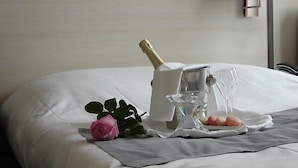 Ein ordentlich bezogenes Bett mit einer Champagnerflasche, einem Glas und einer Rose auf einem Tablett.