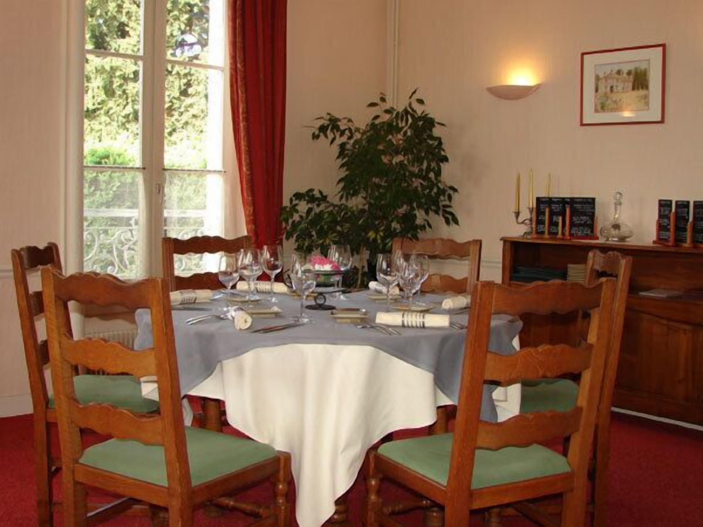 A dining room with a table set for four, surrounded by wooden chairs with green cushions.