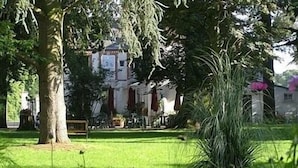 Ein üppiger Garten mit einem großen Baum, einem gepflegten Rasen und einem Gebäude im Hintergrund.
